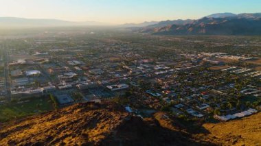 Wide aerial view of Palm Springs, California, captured at sunrise on July 22, 2025. The drone reveals the citys grid layout, residential and commercial zones, and surrounding desert mountains softly