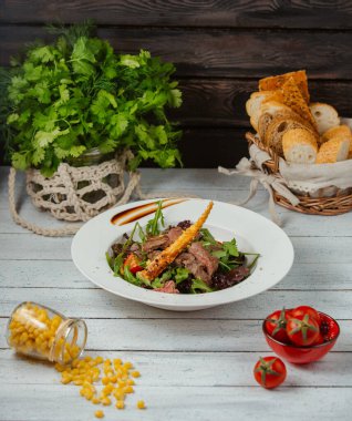 Hafif arkaplanda roka, domates, marul ve ekmek çubuğu ile sığır eti salatası