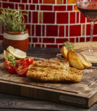 Tahtada kızarmış patates, limon ve domatesle servis edilen kızarmış tavuk köftesi.