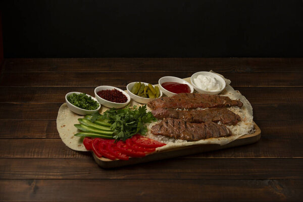 beef fillet kebab slices on rice, served with tomato, cucumber, herbs, sauces