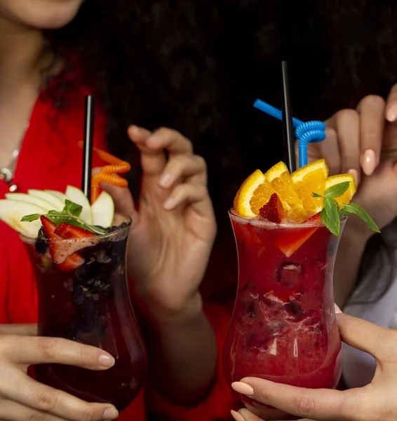 Two woman holding glasses of fruit cocktails with orange, strawberry and apple, strawberry — ストック写真