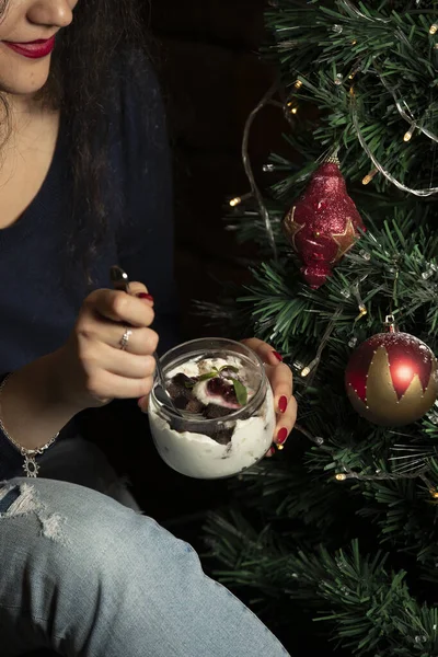 woman eating chocolate cubes in cream in glass jar near christmas tree