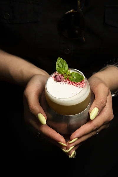 woman hold with both hands glass of drink garnished with dried rose buds