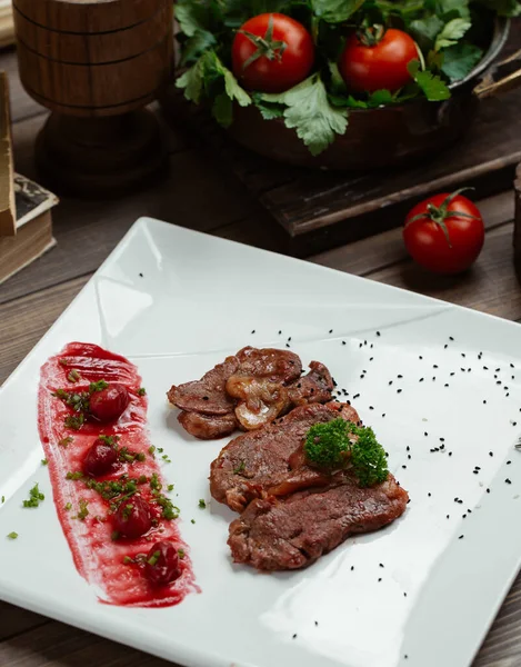 Fette di bistecca di agnello con ciliegia corniola e salsa su piatto quadrato bianco — Foto Stock