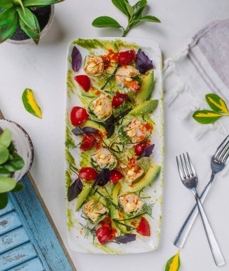 Avokado dilimleri ve vişneli domatesle süslenmiş bir tabak börek.