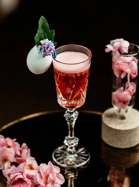 Jasnoczerwony napój w kryształowej szklance ze stojakiem ozdobionym kwiatami — Zdjęcie stockowe