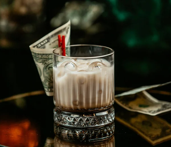 Bebida lechosa con cubitos de hielo en vaso de whisky pinchado con dólar —  Fotos de Stock