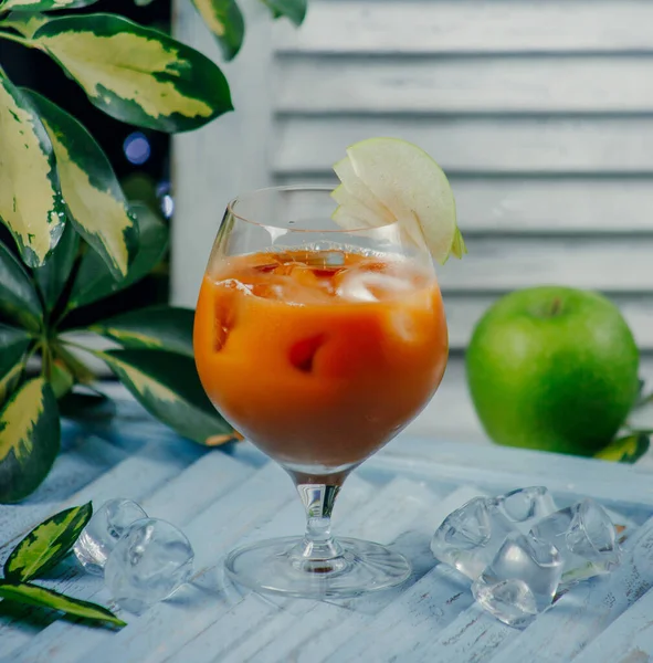 Peach juice in glass with ice cubes and apple slices — Stock Photo, Image