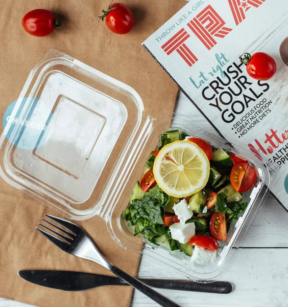 a plastic box of food delivery with greek salad and lemon, diet food