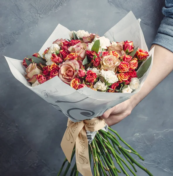 Férfi gazdaság rózsa csokor vörös és sárga kis rózsa, halvány rózsaszín rózsa — Stock Fotó