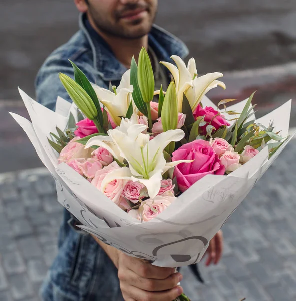 Beyaz zambak buketi ve pembe güller tutan adam.