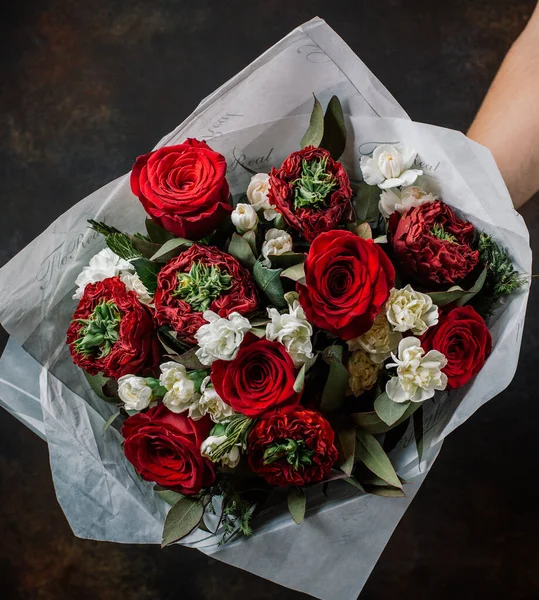 mans hand holds flower bouquet with red roses, white flowers