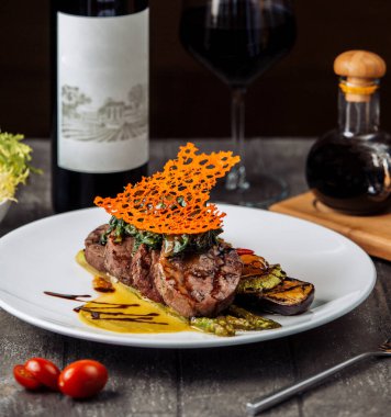 Biftek dilimleri otlar ve sosla süslenmiş ızgara sebzelerle servis ediliyor.