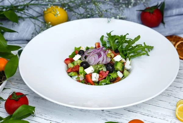Ensalada griega rematada con cebolla roja y rúcula en plato de espaguetis —  Fotos de Stock