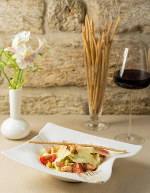 Ekmek çubuğuyla süslenmiş kırmızı şarap kadehiyle servis edilen karides sezar salatası.