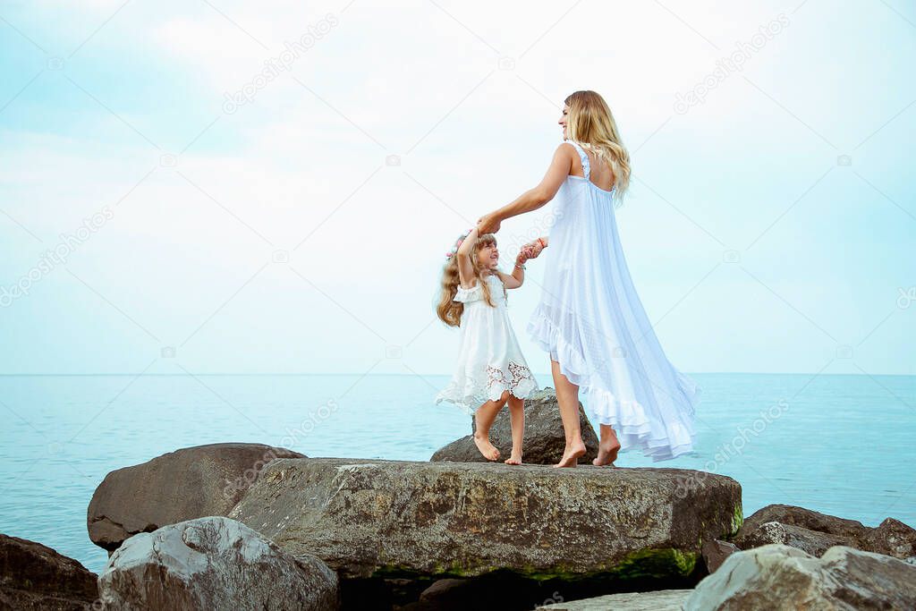 Happy family, mother and daughter spend time on big rocks, on a wild beach near the sea