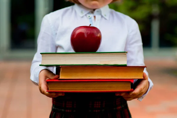 一个穿着白衬衫的女孩拿着一堆有红色苹果的书 — 图库照片