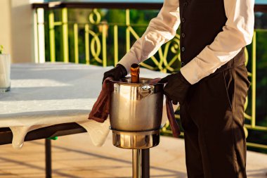 Bir kova soğuk şampanya, üniformalı bir garson ve siyah lateks eldivenler.