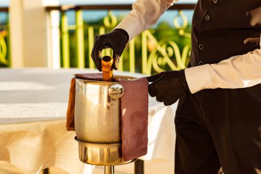 Bir kova soğuk şampanya, üniformalı bir garson ve siyah lateks eldivenler.