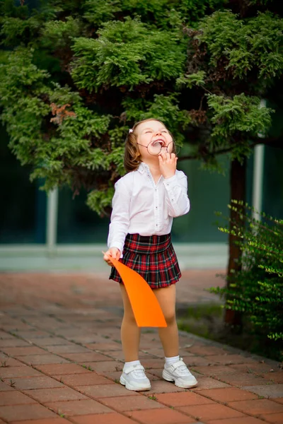 Okul üniformalı bir kız okulun yanında duruyor, elinde bir kağıt parçası, mesaj atmak için yeri olan bir düzen. — Stok fotoğraf