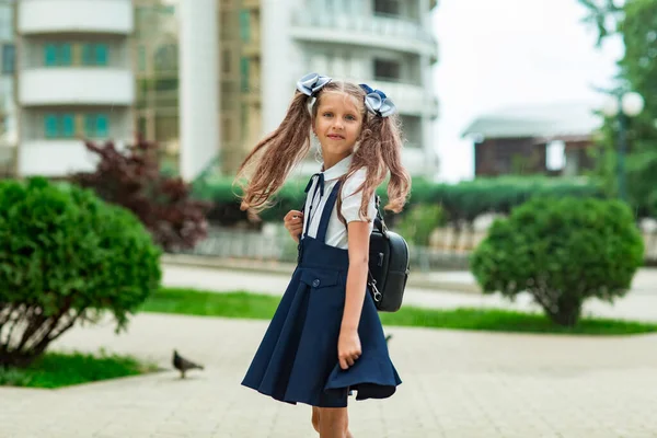 Een mooi meisje, in een blauw schooluniform, met een schoolrugzak, vlakbij het schoolgebouw. Terug naar school, 1 september — Stockfoto