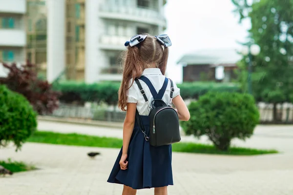Ένα όμορφο κορίτσι, με μπλε σχολική στολή, με σχολική τσάντα, κοντά στο κτίριο του σχολείου. Επιστροφή στο σχολείο, 1 Σεπτεμβρίου — Φωτογραφία Αρχείου