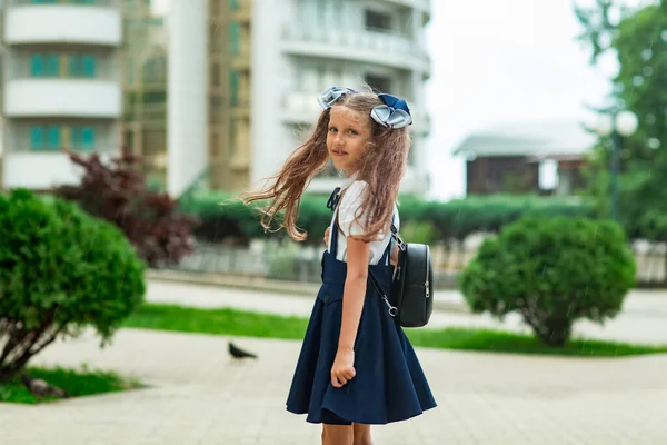 A beautiful girl, in a blue school uniform, with a school backpack, near the school building. Return to school, September 1 — Stock Photo, Image