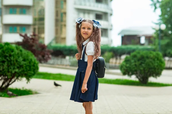 Güzel bir kız, mavi okul üniformalı, okul çantalı, okul binasının yanında. 1 Eylül 'de okula dön.