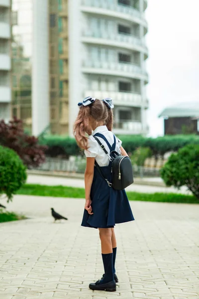 Krásná dívka v modré školní uniformě, se školním batohem, poblíž školní budovy. Návrat do školy, 1. září — Stock fotografie