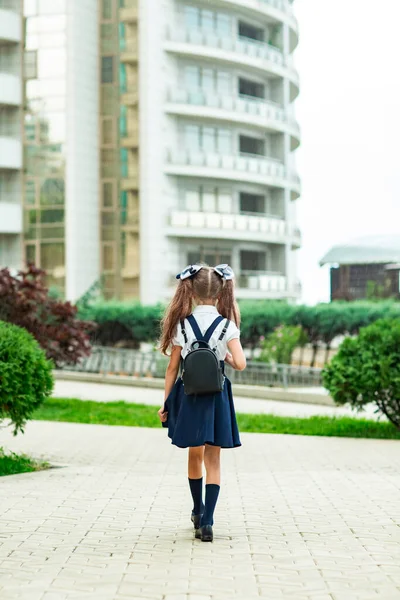 A beautiful girl, in a blue school uniform, with a school backpack, near the school building. Return to school, September 1 — Stock Photo, Image