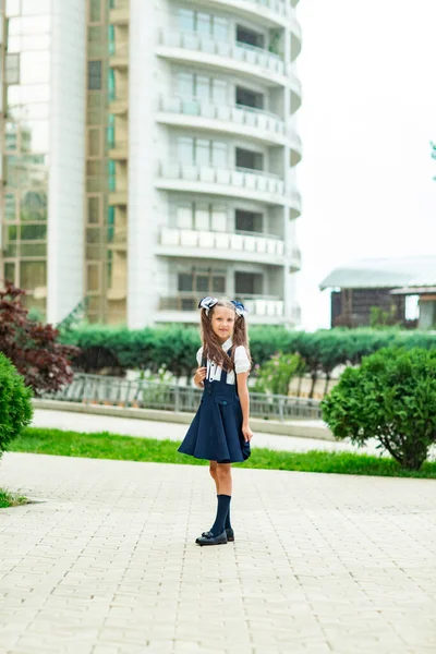 Güzel bir kız, mavi okul üniformalı, okul çantalı, okul binasının yanında. 1 Eylül 'de okula dön.