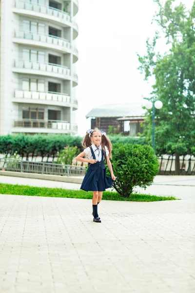 Güzel bir kız, mavi okul üniformalı, okul çantalı, okul binasının yanında. 1 Eylül 'de okula dön.