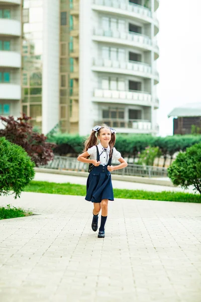 Uma menina bonita, de uniforme azul, com mochila escolar, perto do prédio da escola. Regresso à escola, 1 de Setembro — Fotografia de Stock