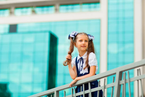 二つのポニーテールを持つ青い学校の制服の女子学生は ガラスの壁で 学校の背景に立っています — ストック写真