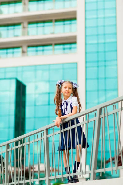 二つのポニーテールを持つ青い学校の制服の女子学生は ガラスの壁で 学校の背景に立っています — ストック写真