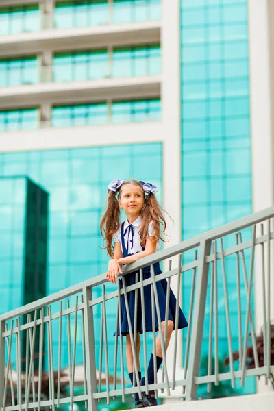 二つのポニーテールを持つ青い学校の制服の女子学生は ガラスの壁で 学校の背景に立っています — ストック写真