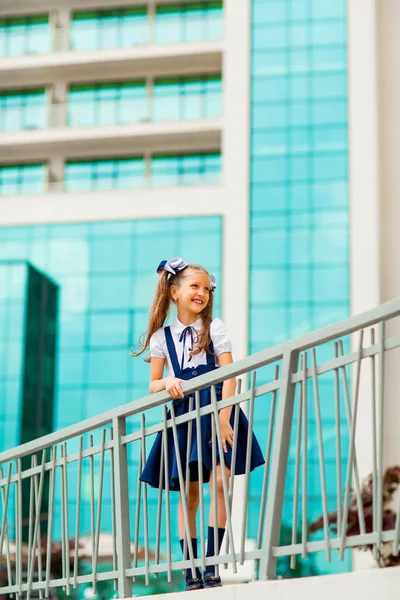 二つのポニーテールを持つ青い学校の制服の女子学生は ガラスの壁で 学校の背景に立っています — ストック写真