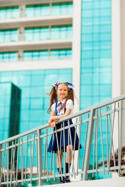 二つのポニーテールを持つ青い学校の制服の女子学生は ガラスの壁で 学校の背景に立っています — ストック写真