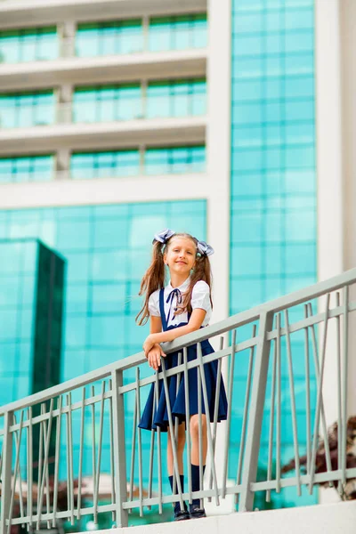 二つのポニーテールを持つ青い学校の制服の女子学生は ガラスの壁で 学校の背景に立っています — ストック写真