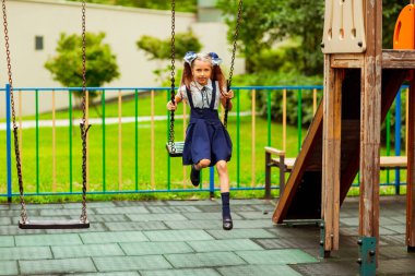 Okul üniformalı kız çocuk parkında salıncakta sallanıyor.