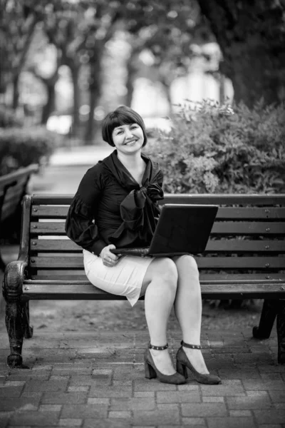 black and white portrait of a woman in business style, with a laptop, on a bench in the Park, working remotely in the field of Economics and accounting.Freelance