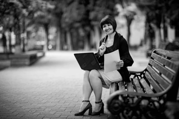 black and white portrait of a woman in business style, with a laptop, on a bench in the Park, working remotely in the field of Economics and accounting.Freelance