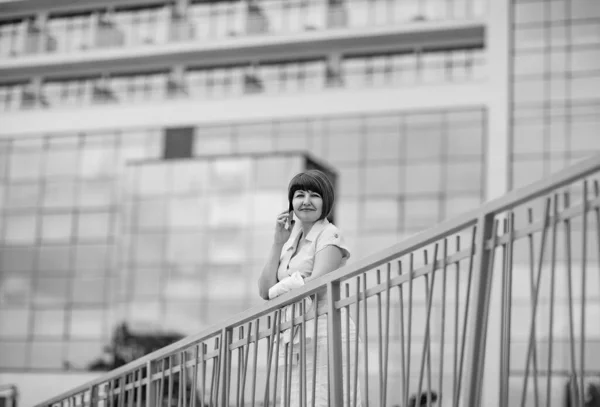 black and white portrait of a woman, in business style, with a mobile phone in her hand, against the background of a glass building, in a big city.business lady