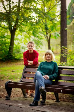 Güzel bir kadın, sarışın, orta yaşlı, oğluyla birlikte parkta bir bankta oturuyor ve iletişim kuruyor.
