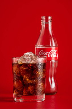 Minsk, Beyaz Rusya - 14 Nisan 2018: Klasik şişe Coca-Cola ve cam buz ve içecek olarak kırmızı arka plan ile. Coca Cola İçecek üretilen ve Coca-Cola Company tarafından üretilen.
