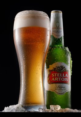 MINSK, BELARUS -MARCH 29, 2018: Cold Bottle and glass of Stella Artois beer on black background, prominent brand of Anheuser-Busch InBev, is a pilsner brewed in Leuven, Belgium, since 1926 clipart