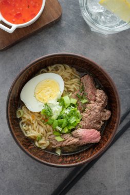 Sığır eti, yumurta, chives kase gri arka plan üzerinde Asya ramen çorbası