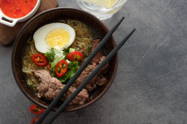 Sığır eti, yumurta, kase gri arka plan üzerinde chives ile Asya ramen çorbası. Boşaltmak. Üstten görünüm.