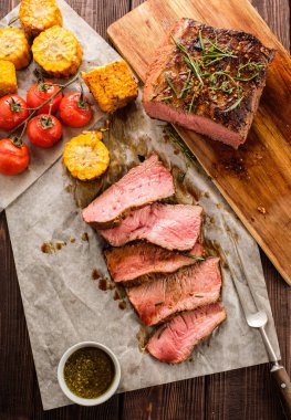 Üzerinde kesme tahtası ızgara sebzeli biftek dilimlenmiş. Üstten görünüm.