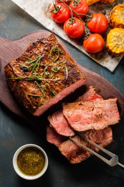 Üzerinde kesme tahtası ızgara sebzeli biftek dilimlenmiş. Üstten görünüm.